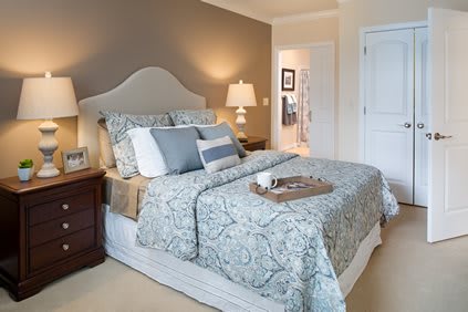 A cozy bedroom featuring a neatly made bed with patterned bedding, accompanied by nightstands and lamps on either side.