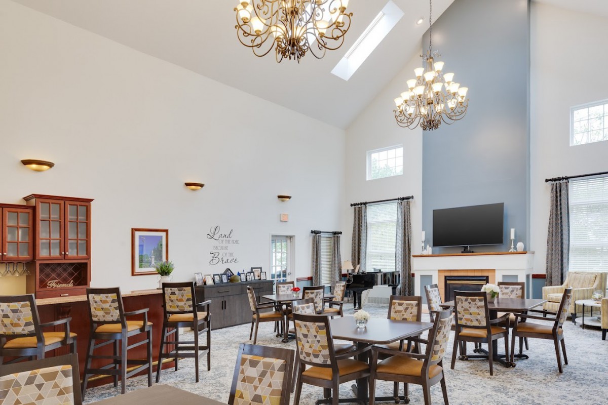 A spacious dining room with elegant chandeliers, round tables, and a cozy fireplace.