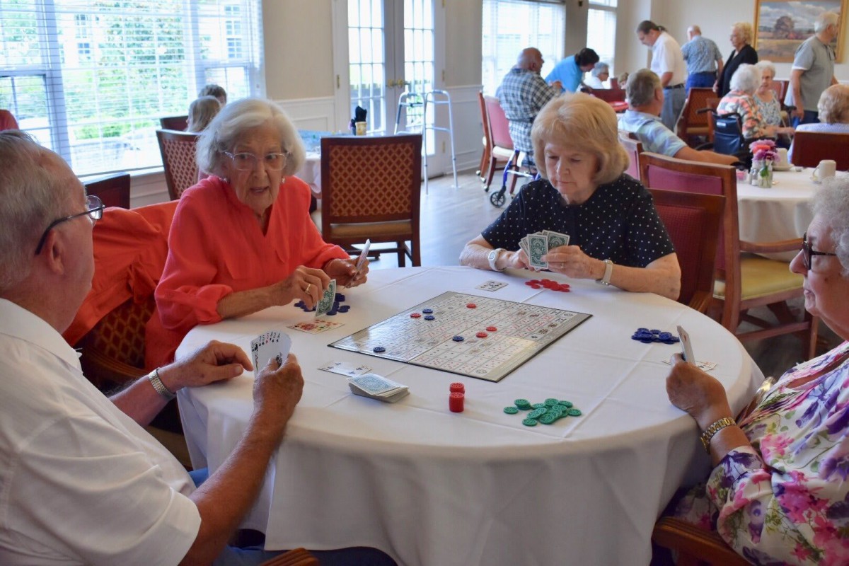 A group of seniors enjoying a card game around a table in a communal setting.