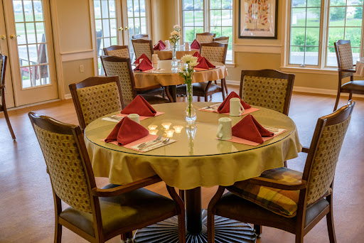 A beautifully arranged dining area ready for guests, featuring elegant table settings with red napkins and a floral centerpiece.