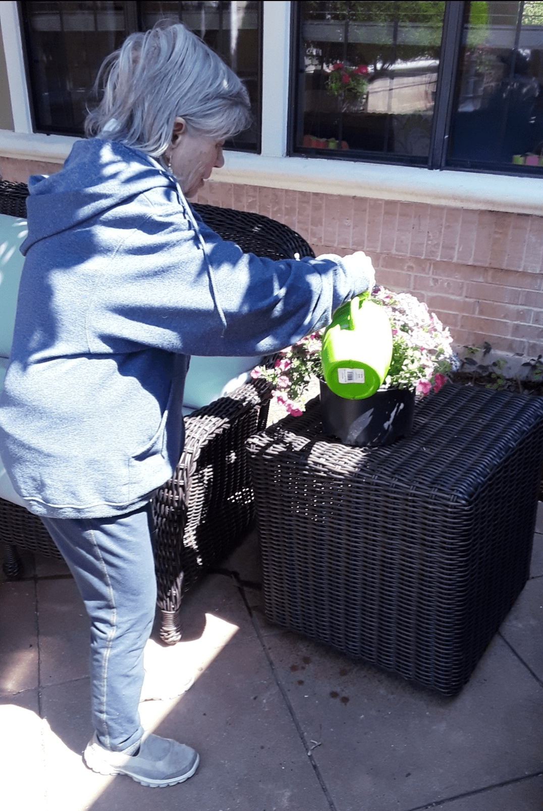 A person is watering plants outdoors with a green watering can.