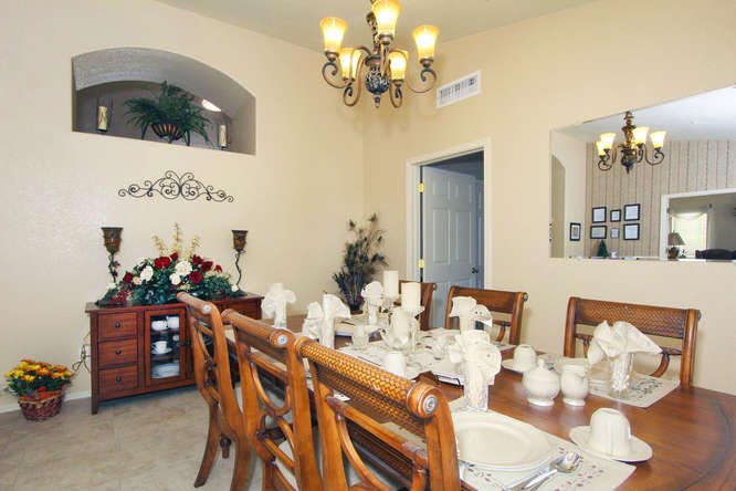 A well-decorated dining room with a large wooden table and matching chairs, adorned with elegant table settings and a chandelier overhead.