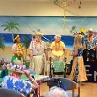 A group of elderly people dressed in Hawaiian-themed attire, enjoying a tropical party with colorful decorations.