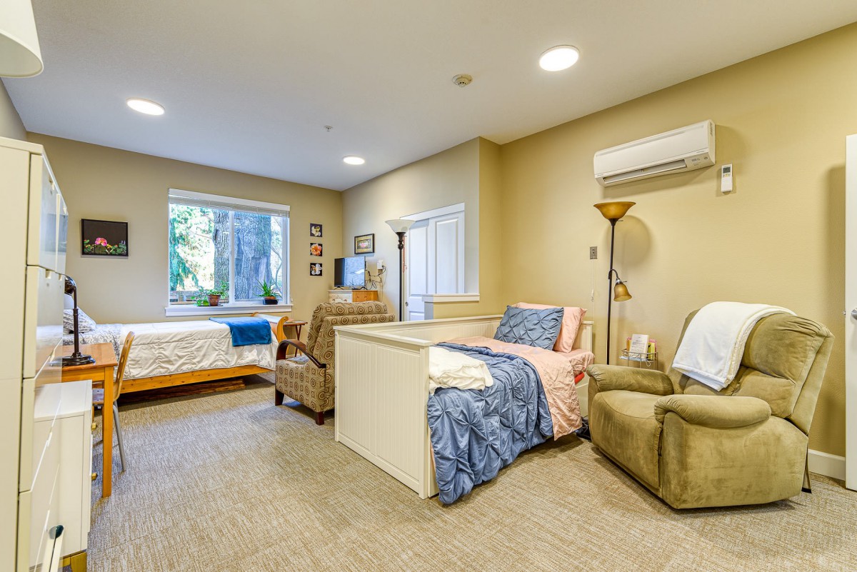 A cozy and well-furnished bedroom interior with two beds, chairs, a window, and a lamp.