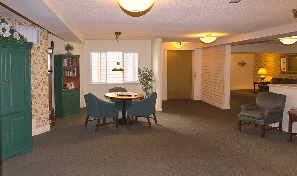 A cozy interior space with a table and chairs, a bookcase, and warm lighting.