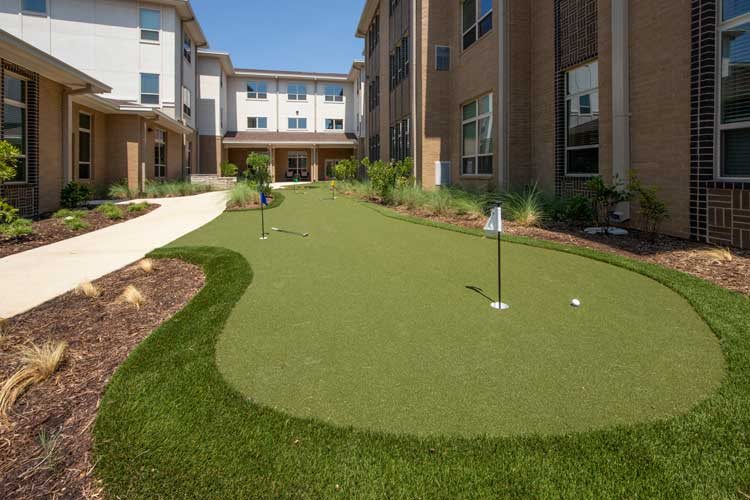 An outdoor putting green situated next to a building, offering a recreational space for golf enthusiasts.