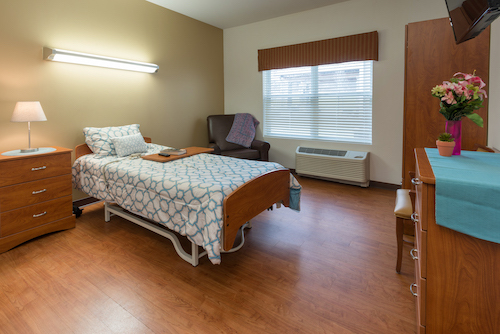 A well-lit hospital room featuring a single bed, comfortable chair, and window.