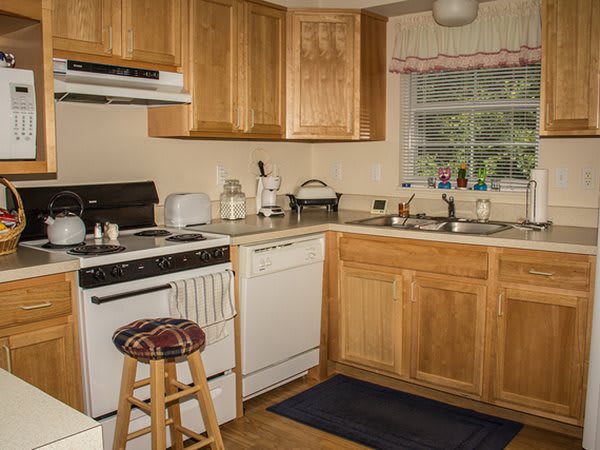 A cozy kitchen with wooden cabinets, featuring an oven, dishwasher, and a window overlooking the outside.