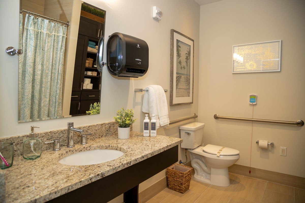 A well-organized bathroom with a granite countertop, featuring a sink, toilet, mirror, and decor items.