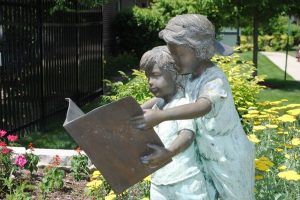 A statue of two children reading a book together in a garden setting.