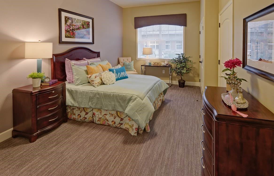 A cozy bedroom interior with a large bed, nightstands, and warm lighting.