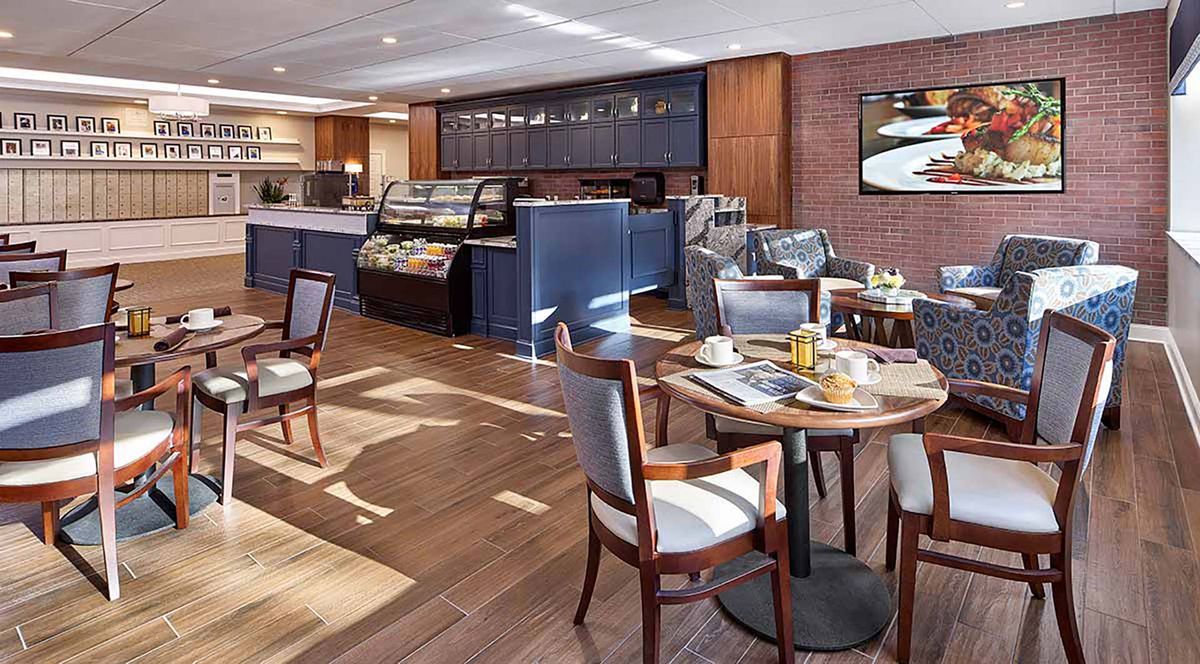 A cozy cafe interior with tables, chairs, and a counter with food display.
