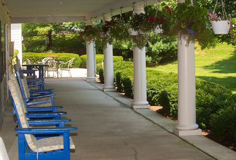 A porch with columns and blue chairs overlooking a garden.