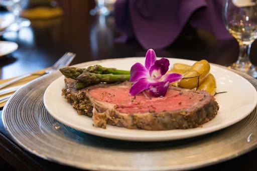 A beautifully plated dinner featuring a juicy steak, asparagus, and a decorative purple flower.