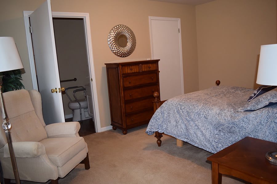 A cozy bedroom with a dresser, bed, and armchair.