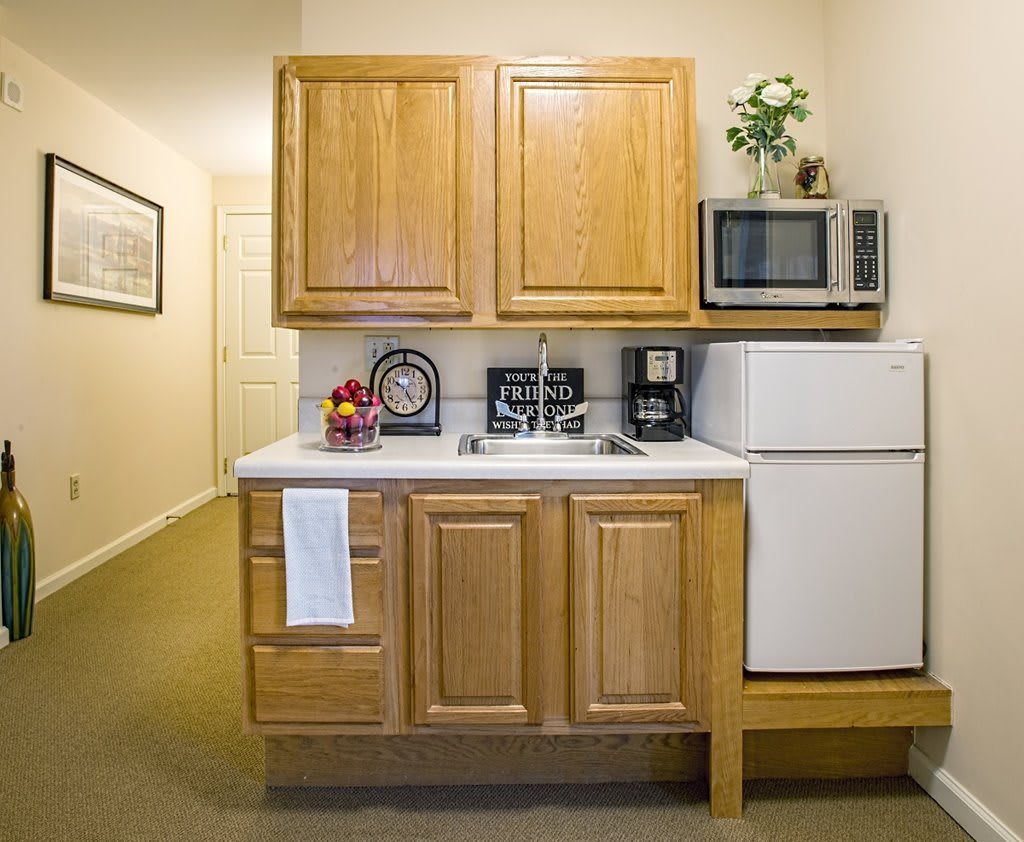 A small kitchenette with wooden cabinets, a microwave, refrigerator, and coffee maker.