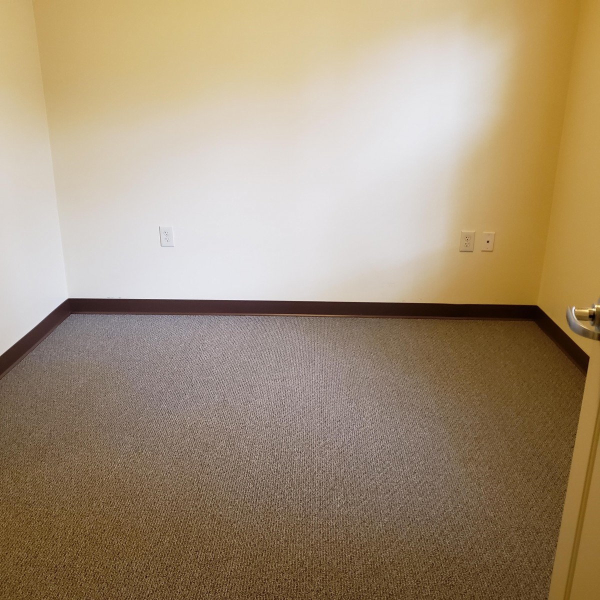 An empty room with beige walls and a carpeted floor.