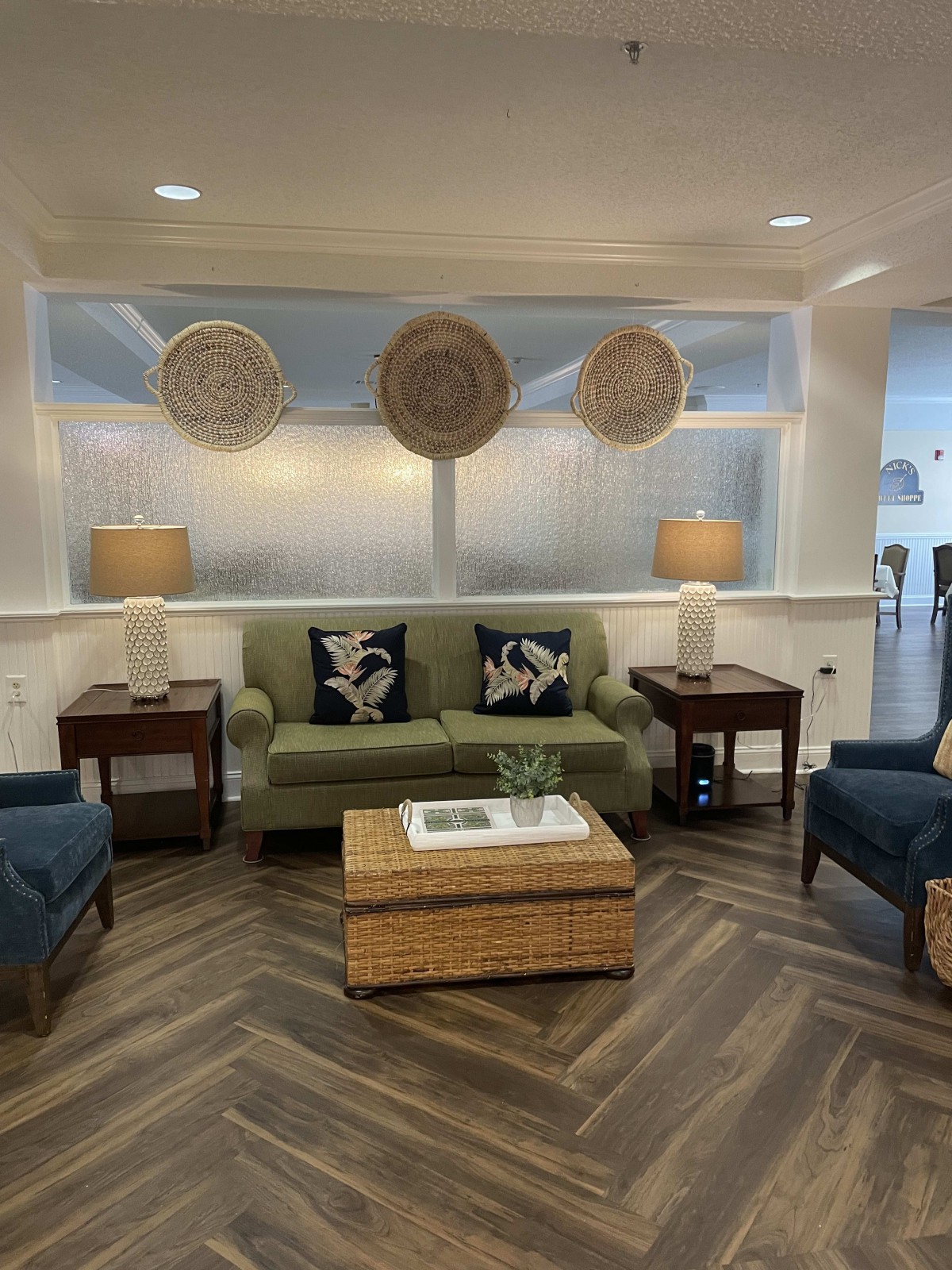 A cozy living room with a green sofa, two blue armchairs, and a wicker coffee table, enhanced by stylish decor and warm lighting.