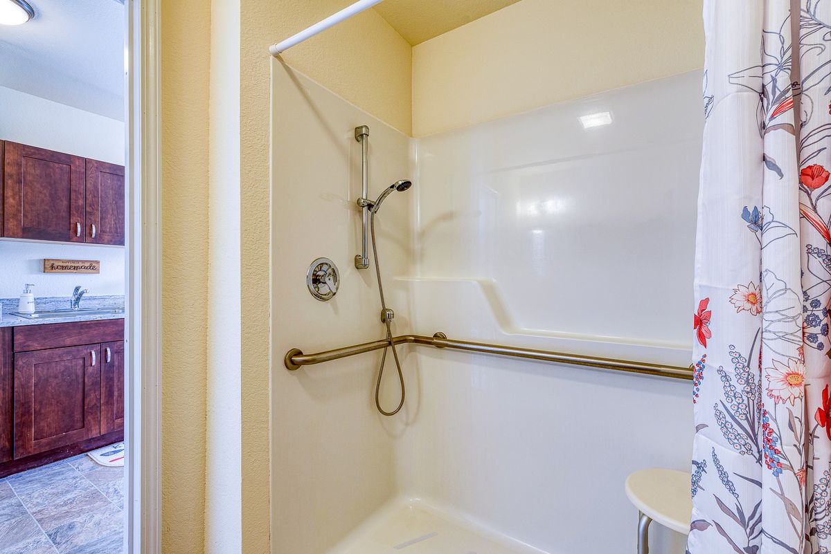 A bathroom with a walk-in shower featuring a handheld showerhead and safety grab bar.
