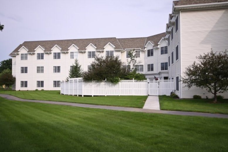 A residential apartment building with manicured lawn and white fencing.