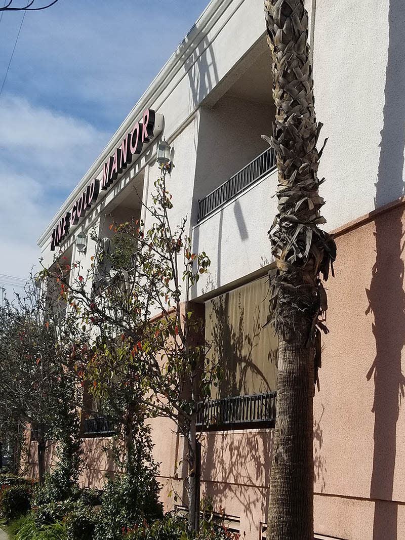 A building with a sign and trees in front on a sunny day.
