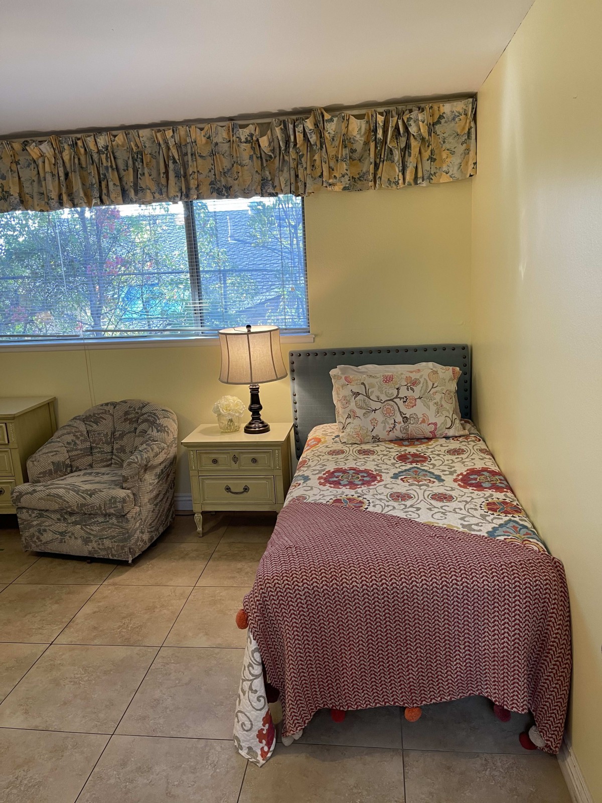 A cozy bedroom with a single bed, armchair, and a lit lamp on the nightstand.