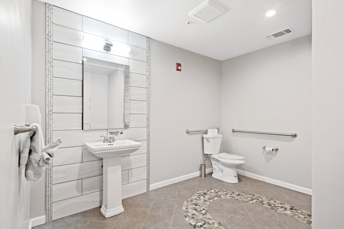 A modern and minimalist bathroom with a sink, mirror, and toilet on white walls.