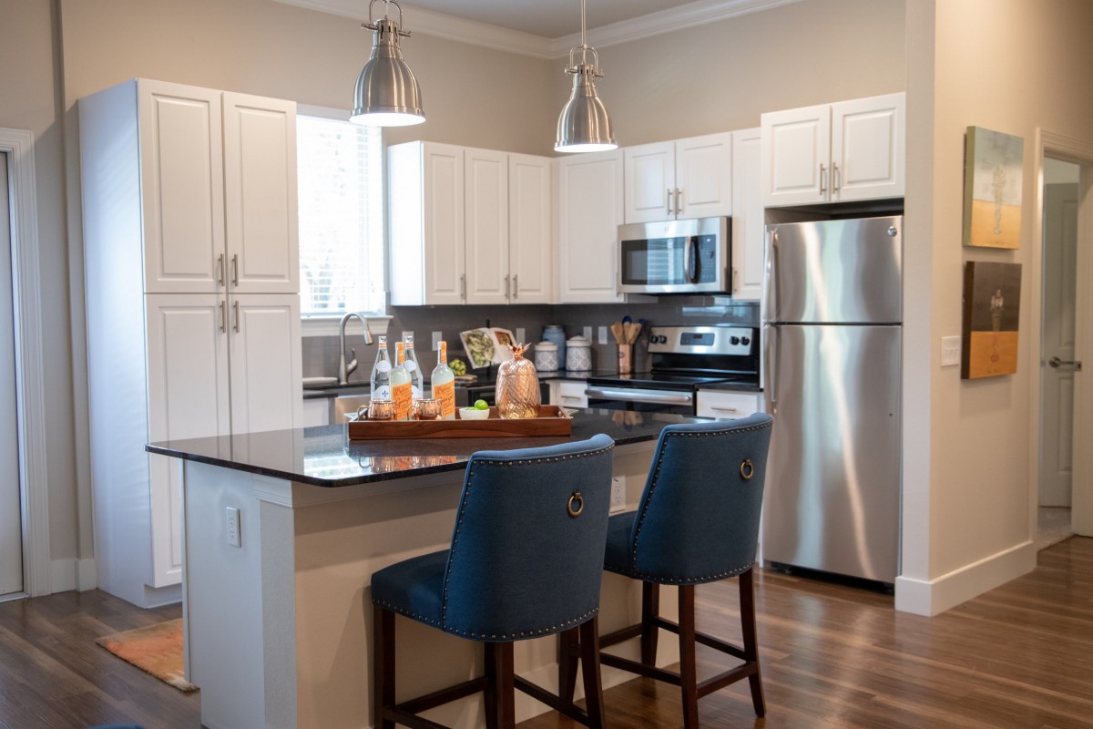 A modern kitchen with white cabinets, a stainless steel refrigerator, and an island with two blue chairs.