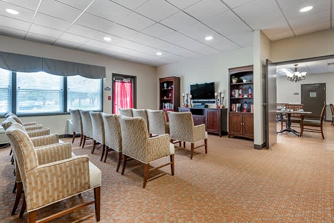 A well-lit waiting room with rows of chairs facing a television and bookshelves.