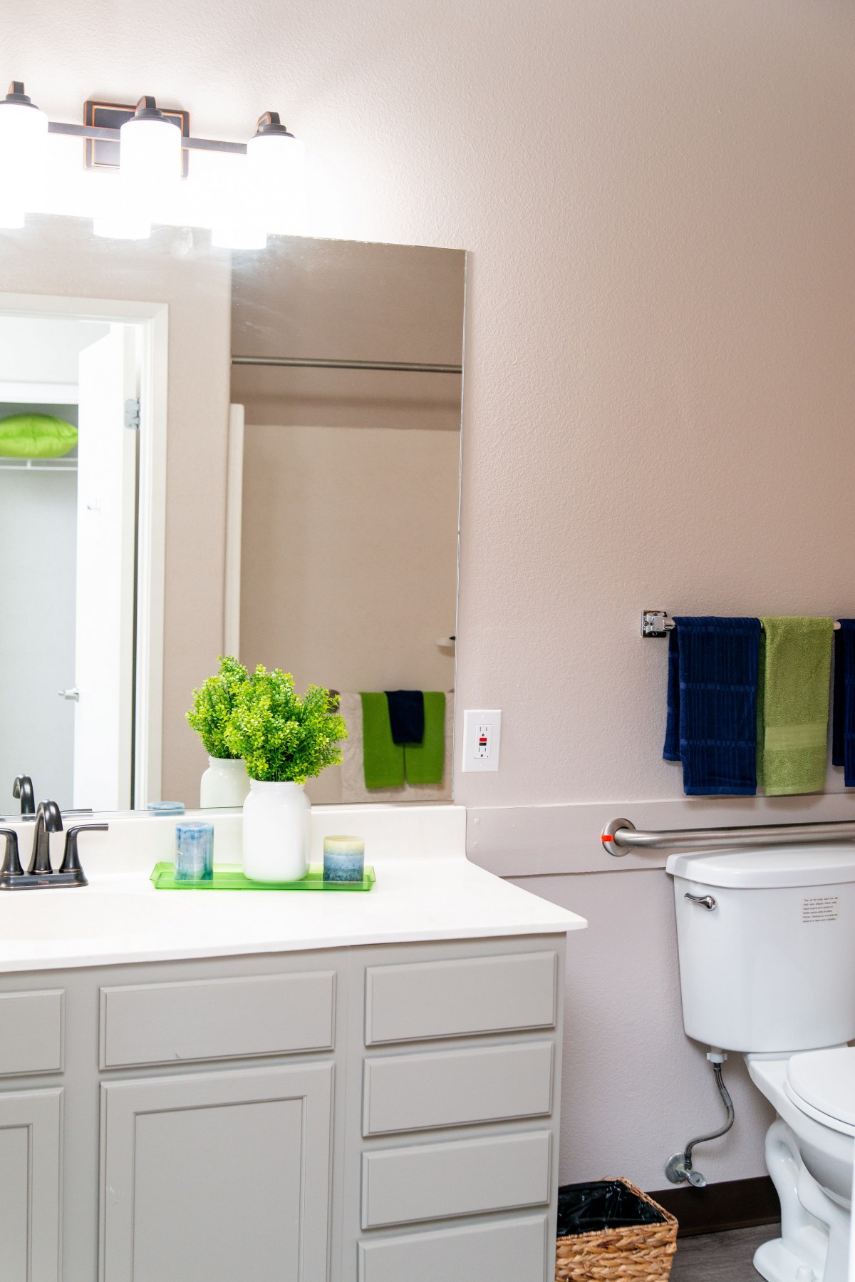 A bright and tidy bathroom with a mirror, sink, decorative plants, and neatly arranged towels.