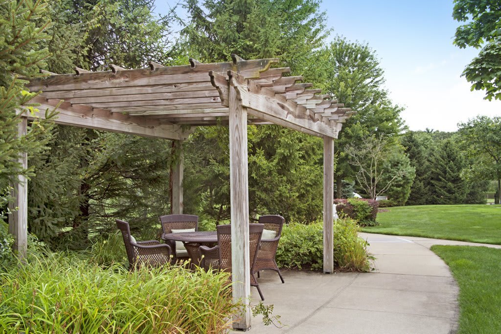 A wooden pergola with patio seating in a lush garden setting.