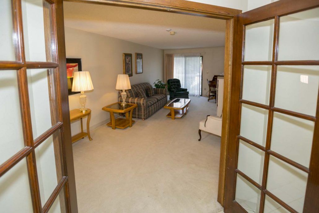 A cozy living room with a sofa, lamps, and a coffee table viewed through glass doors.