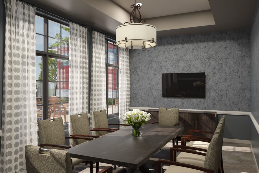 A modern conference room with a large meeting table, chairs, and a wall-mounted television. The room features large windows allowing natural light, a stylish chandelier, and a vase of flowers on the table.