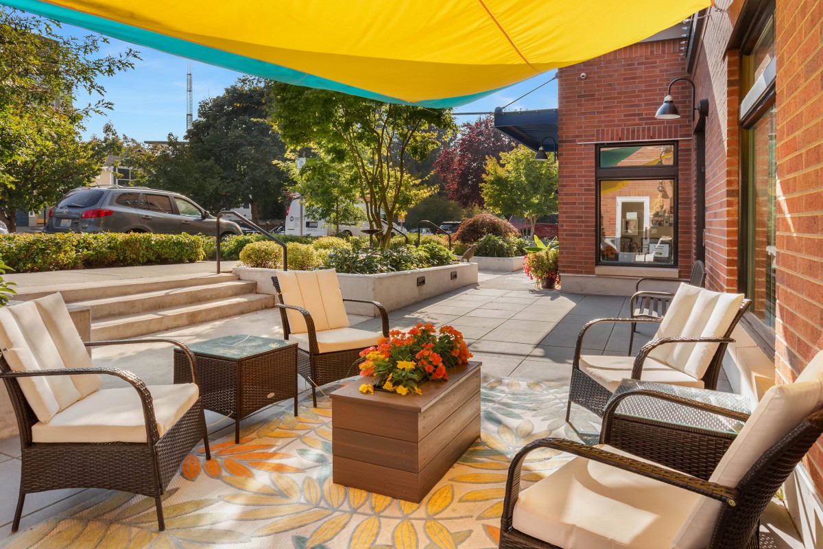 A cozy outdoor patio with comfortable seating under a large, colorful umbrella shade.