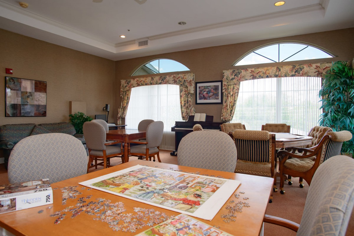 A cozy living room with tables and chairs, featuring a partially completed puzzle.