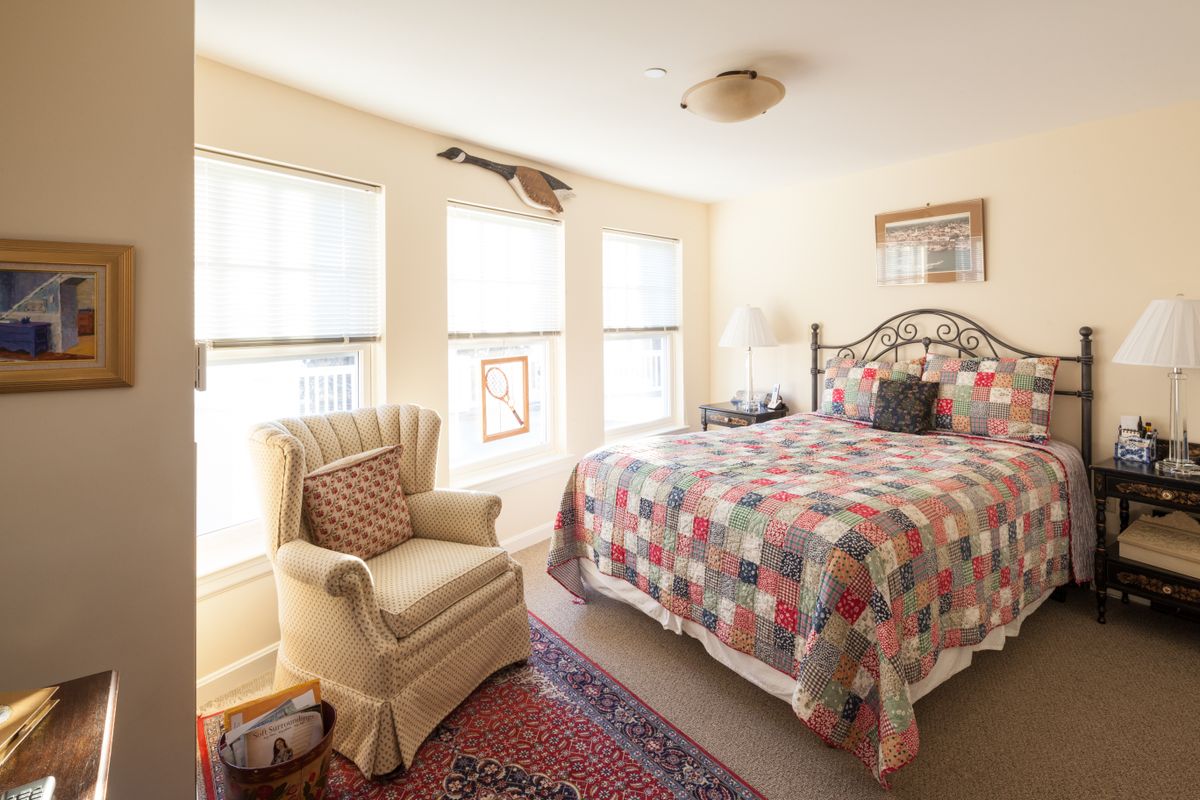 A cozy bedroom with a patterned bedspread, comfortable armchair, and large windows allowing natural light.