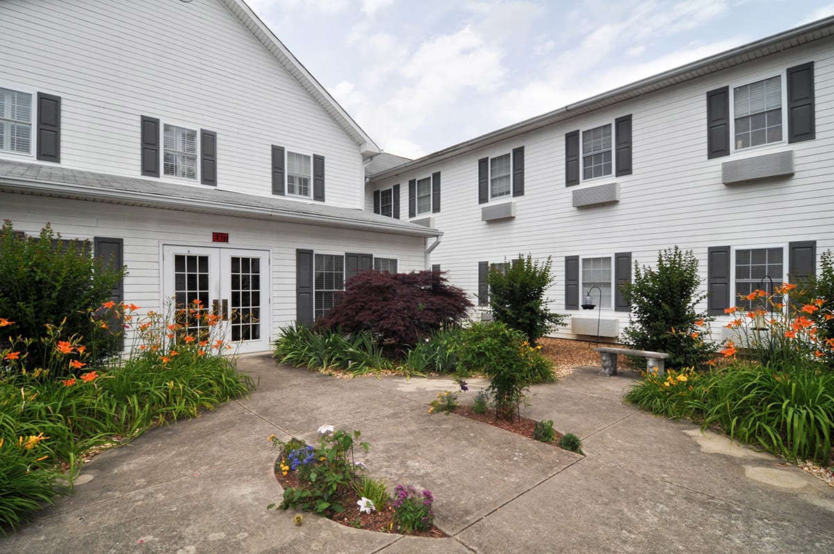 A serene courtyard surrounded by a white building with windows and lush greenery.