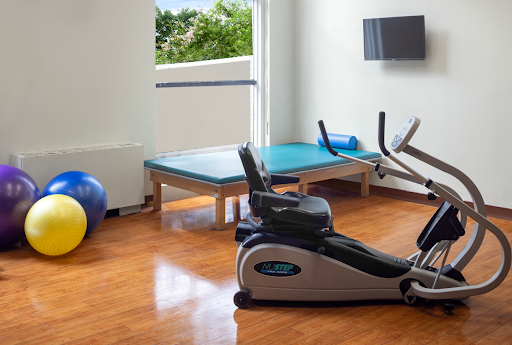 A well-equipped home gym featuring an elliptical machine, exercise ball, and rehabilitation table.