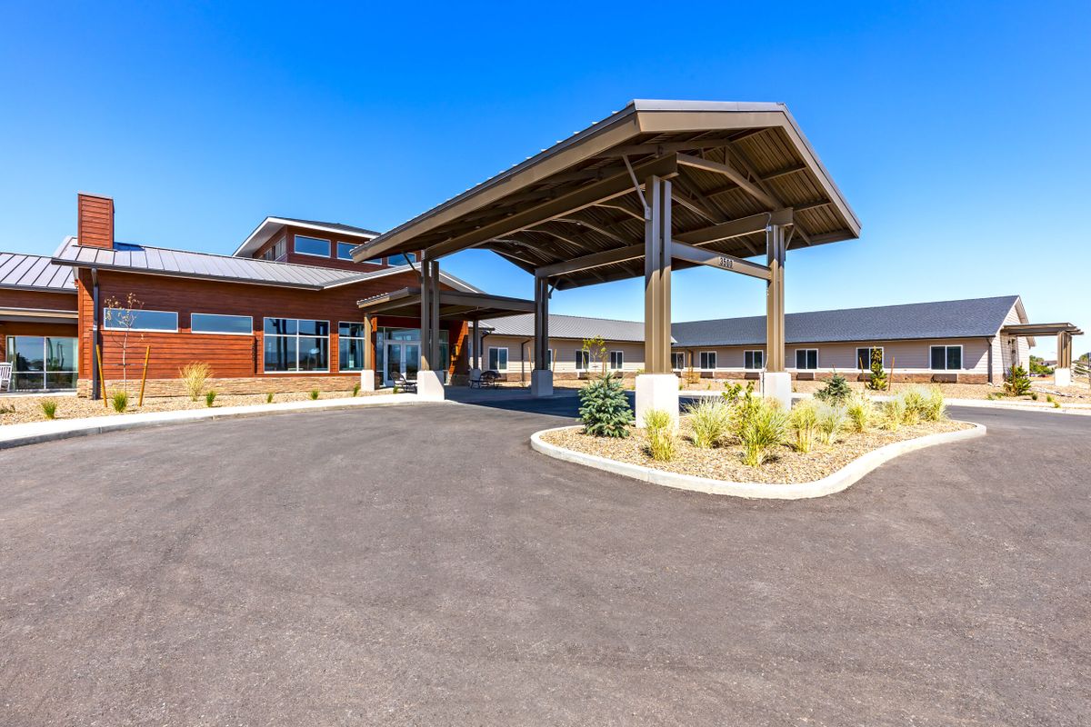A modern building entrance with a covered driveway and landscaped surroundings under a clear blue sky.