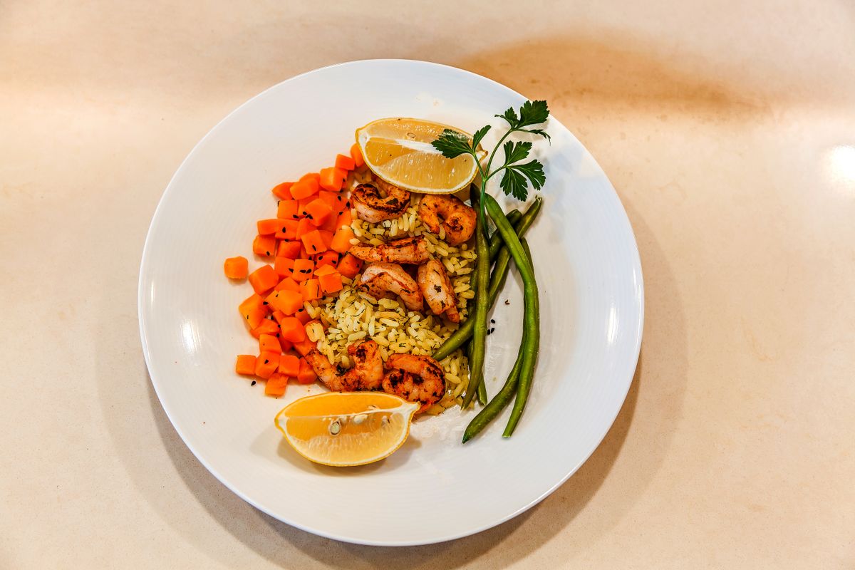 A beautifully plated dish featuring shrimp over rice, accompanied by diced carrots, green beans, and lemon slices.