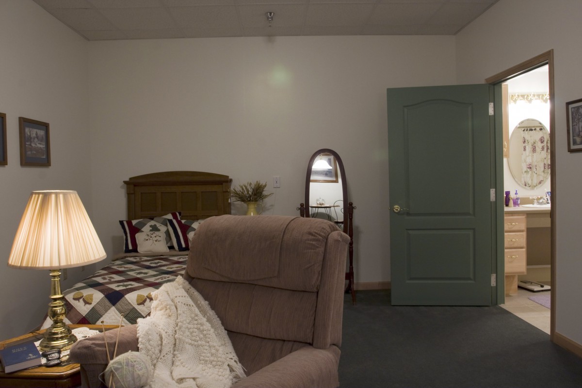 A cozy bedroom with a bed, chair, and mirror.