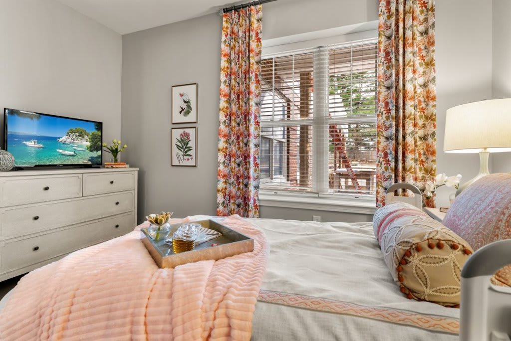 Cozy bedroom with a neatly made bed, colorful curtains, and a tray on the bed near the window.