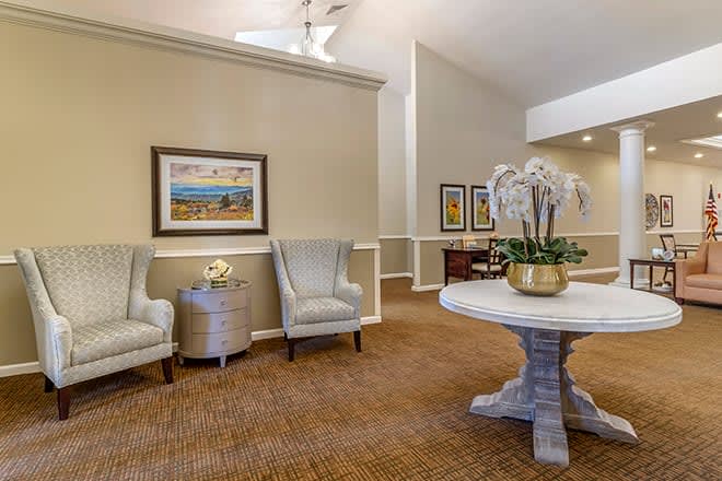 A cozy lobby interior featuring elegant seating, artwork on the walls, and a decorative plant on a central table.