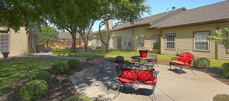 A peaceful outdoor patio area with red-cushioned chairs and tables surrounded by trees.