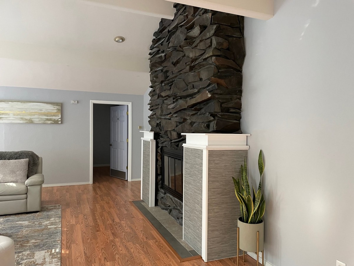 A cozy living room features a striking stone fireplace and hardwood floors, complemented by a potted plant.