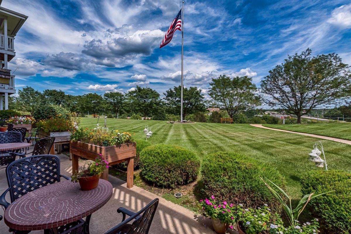 A well-maintained garden with a patio and an American flag under a vibrant, cloudy sky.