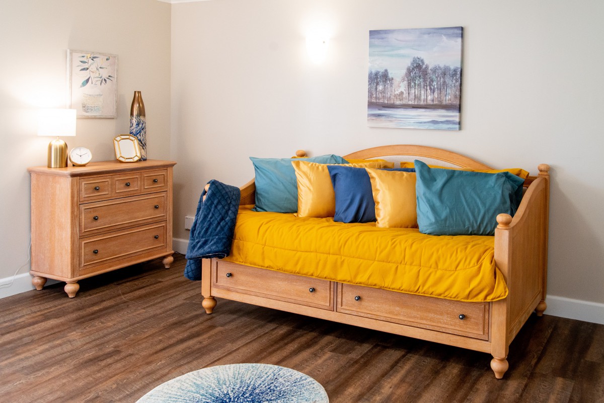 A cozy bedroom featuring a wooden daybed adorned with colorful pillows and matching furniture on a hardwood floor.