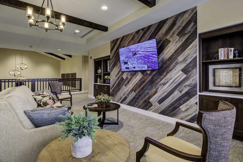 A modern living room with a wood accent wall, mounted television, elegant furniture, and a decorative chandelier.