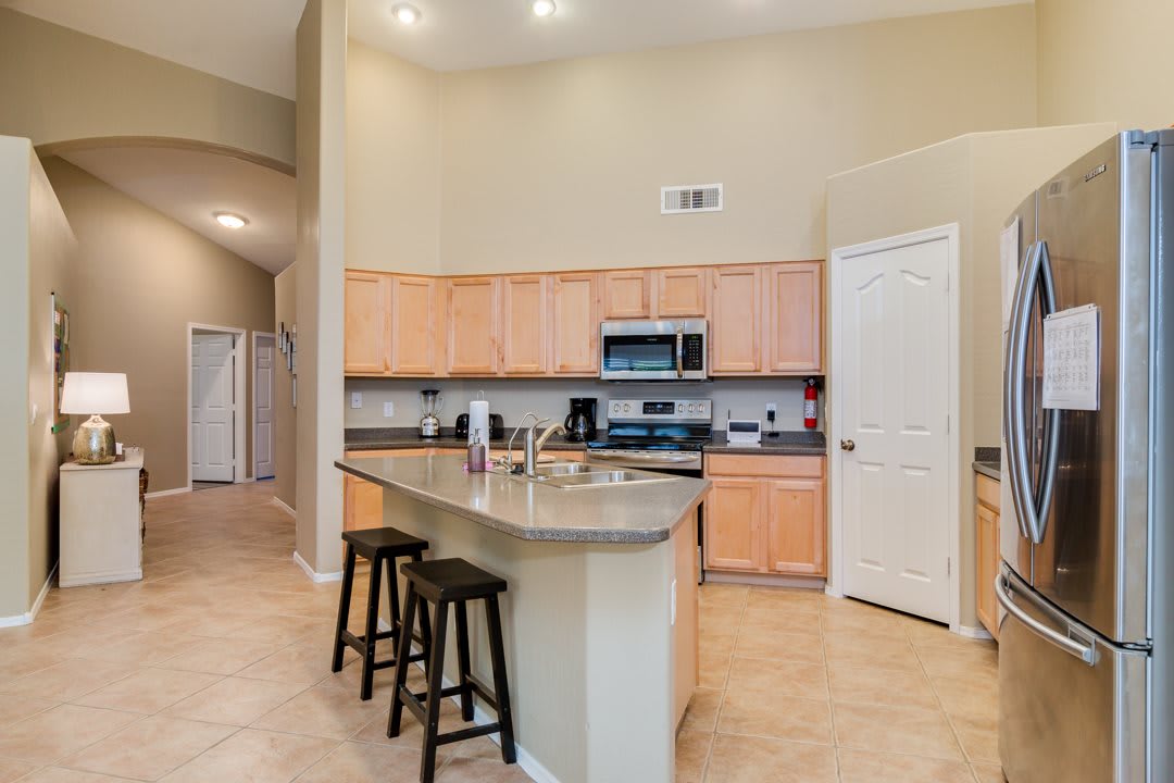 A modern kitchen with an island and bar stools, featuring wooden cabinets and stainless steel appliances.
