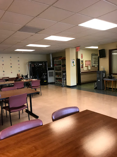 A spacious dining area with tables and chairs, equipped with a kitchenette in the background.